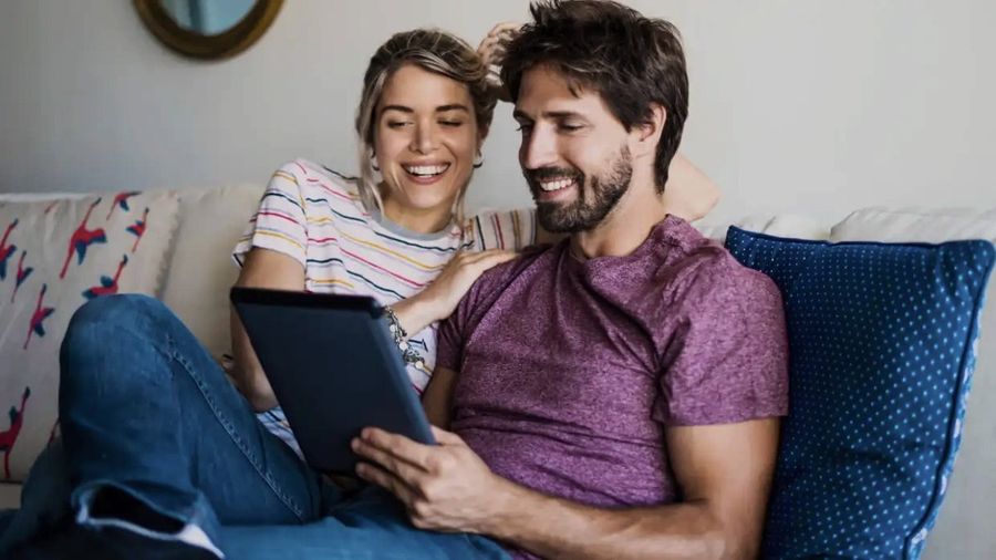 Un couple regarde la télévision sur une tablette, installé dans un canapé